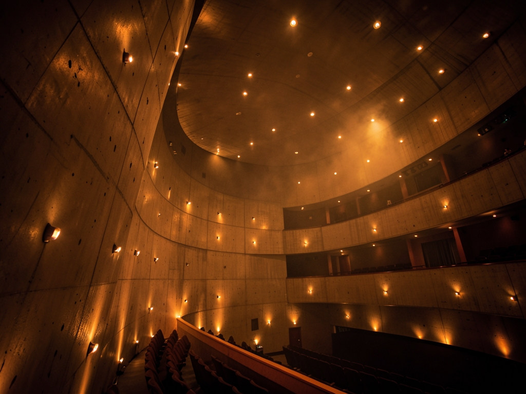 dimly curved concrete concert hall interior soft amber glow