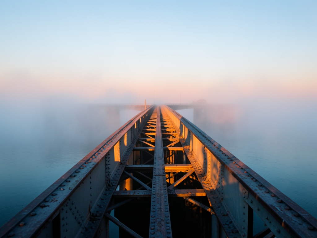 long steel bridge over foggy water dawn only