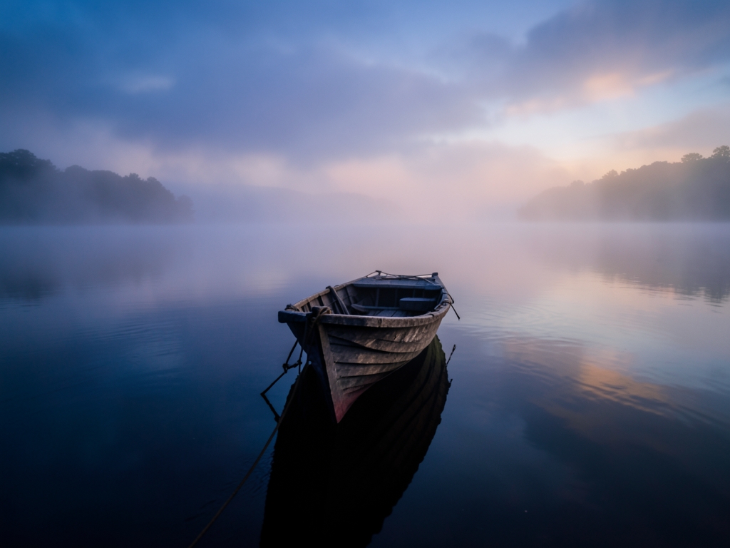narrow wooden boat drifting through mist over vast