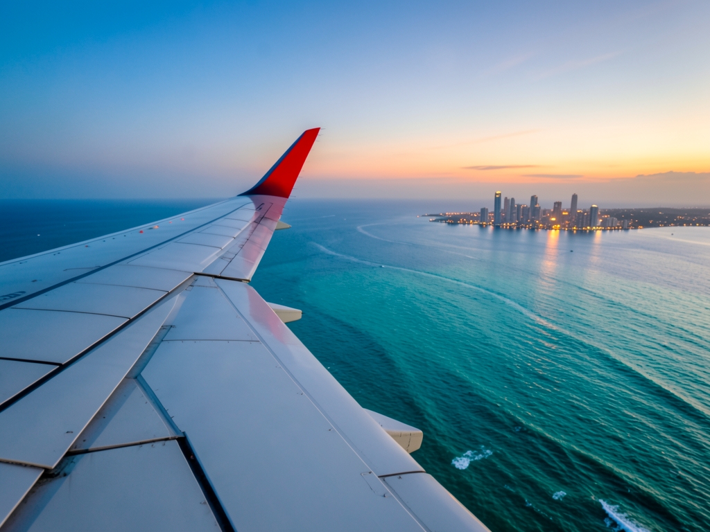 Turquoise ocean beneath high altitude airplane wing dusk distant