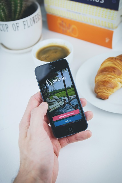 airbnb app apple book coffee croissant hand holding ios iphone mobile phone table white airbnb airbnb airbnb airbnb airbnb